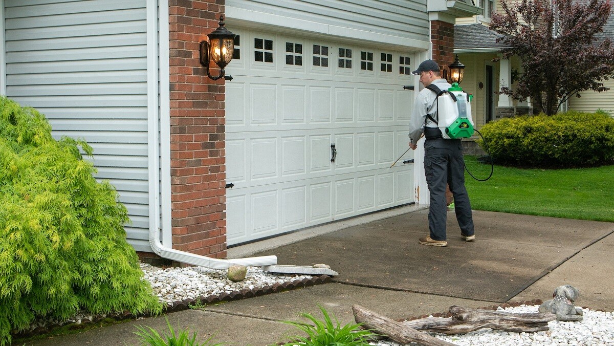 pest control technician spraying outside of house